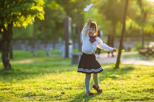 Una niña jugando con un avión de papel en el parque.