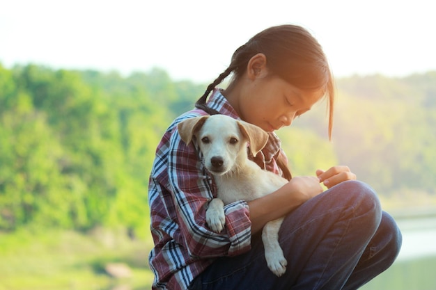 Foto niña jugando con un cachorro sentada en una roca junto al lago contra un cielo despejado