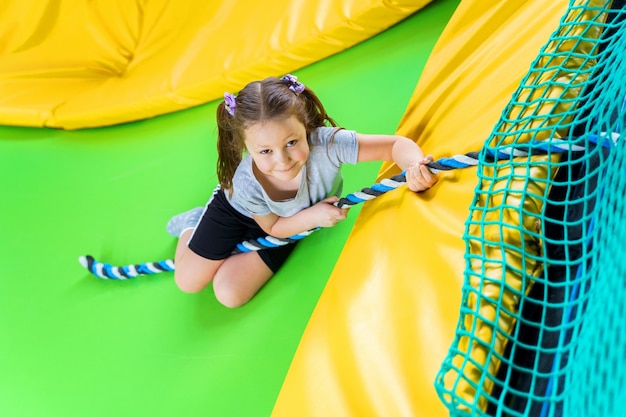 Niña jugando en el centro de trampolín saltando y escalando con una cuerda