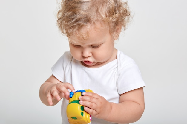 Niña jugando con coche amarillo, mirando coche de juguete con gran interés, vistiendo camiseta