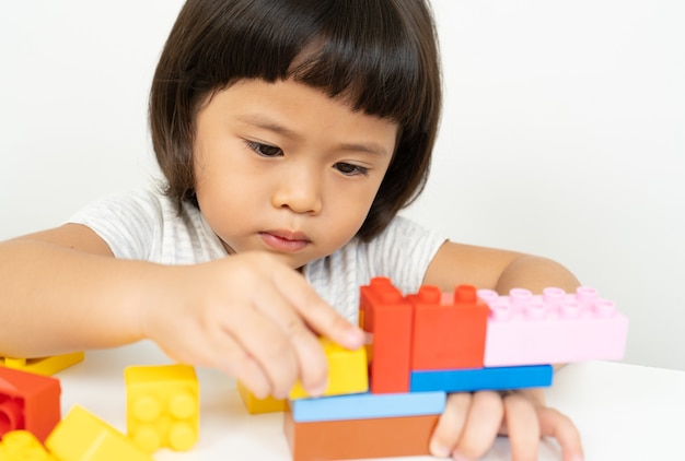 Niña jugando con coloridos bloques de juguete en blanco, los niños juegan con juguetes educativos