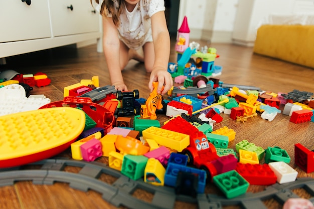 Foto niña jugando con coloridos bloques de juguete. juguetes y juegos educativos y creativos para niños pequeños. tiempo de juego y desorden en la habitación de los niños.