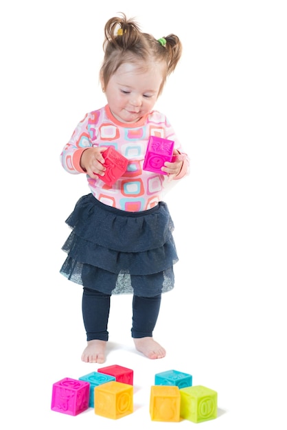 Niña jugando con cubos de colores sobre un fondo blanco.