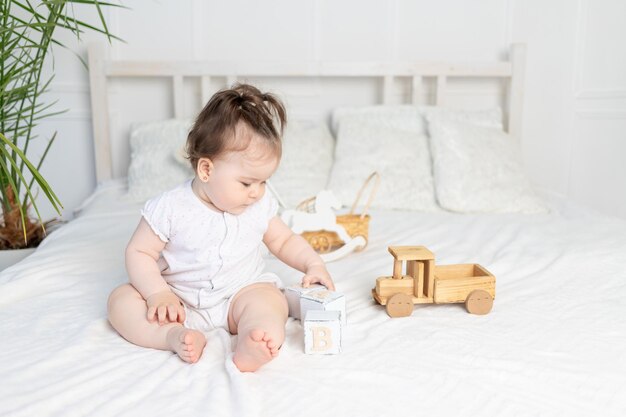 Niña jugando con cubos de juguete de madera en la cama en casa en una habitación luminosa el concepto de desarrollo de la primera infancia