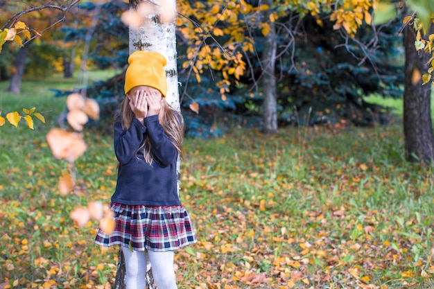 Niña jugando a las escondidas en el bosque de otoño