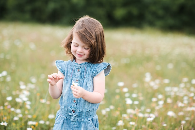 Niña jugando con flores posando en la pradera