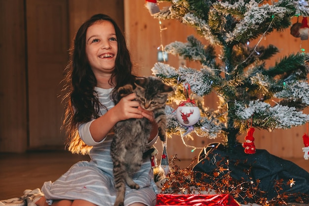 niña jugando con gatito debajo del árbol de navidad