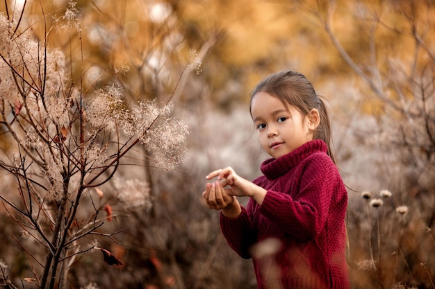 Niña jugando con hojas caídas de otoño