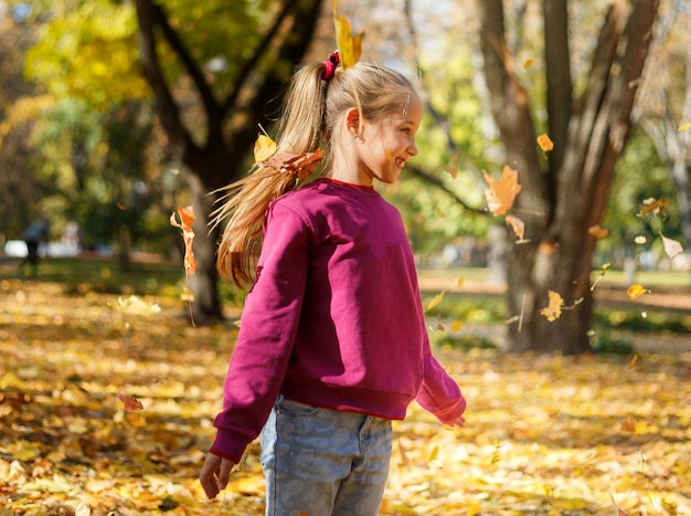 Niña jugando con hojas de otoño en el parque