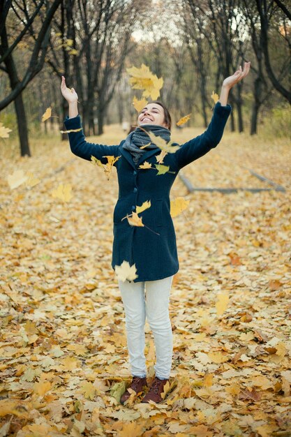 Niña jugando con hojas secas de otoño en el bosque