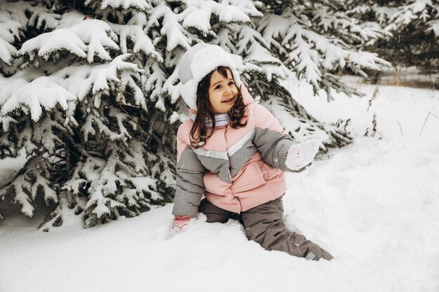 Niña jugando en el invierno en el bosque cubierto de nieve. Hermoso retrato infantil de invierno. Niño feliz, diversión de invierno al aire libre.