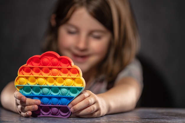 Foto niña jugando con el juguete de silicona pop it de color arcoíris antiestrés.