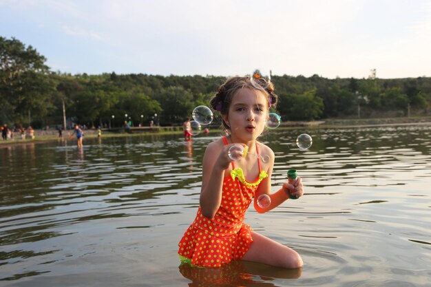 niña jugando en el lago con pompas de jabón