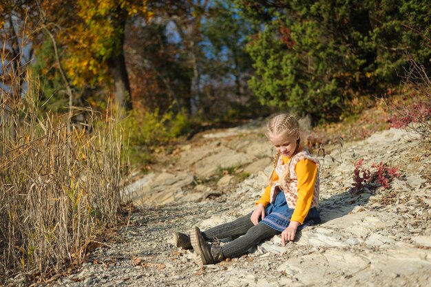 Niña jugando niño en edad preescolar se sienta en el suelo en un claro día soleado de otoño en el bosque