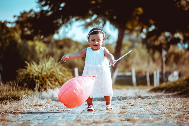 Niña jugando en el parque con globo rosa