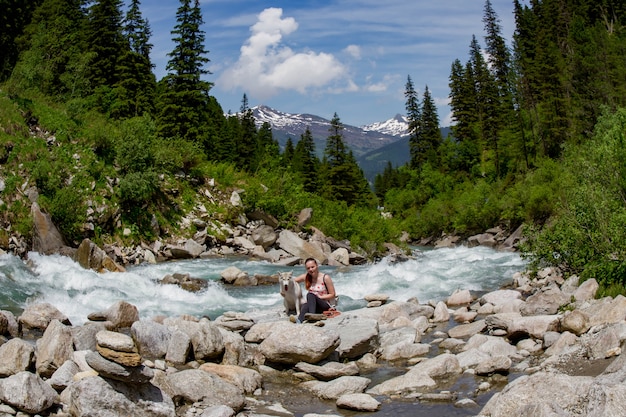 Niña jugando con un perro husky en la orilla de un río de montaña