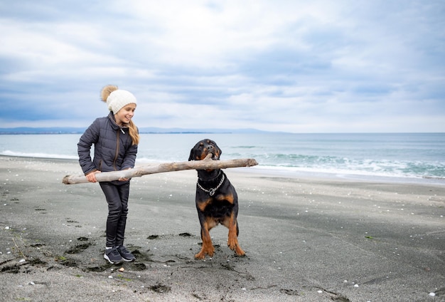 Niña jugando con perro rottweiler en clima frío en la playa