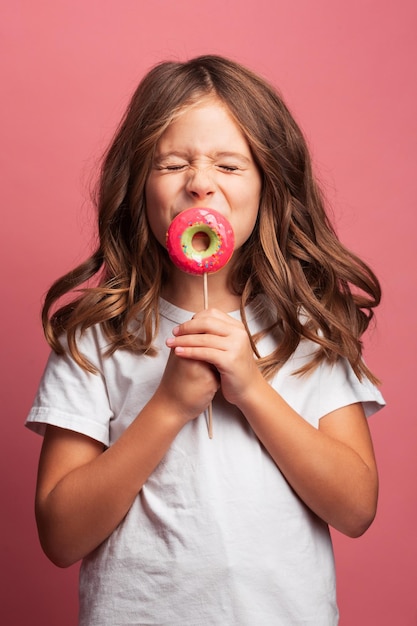 Niña jugando con piruletas en el fondo rosa