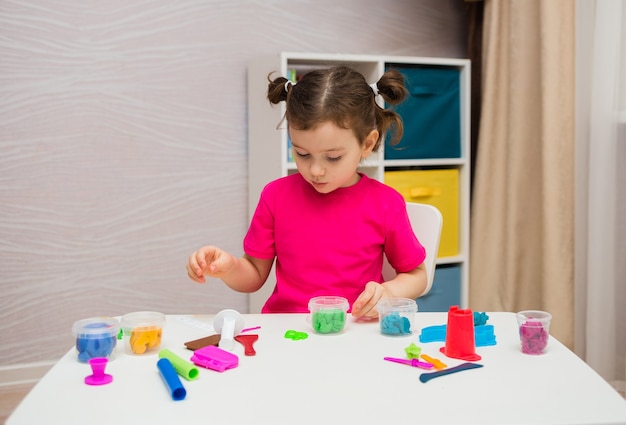 Niña jugando con plastilina en la mesa de la habitación