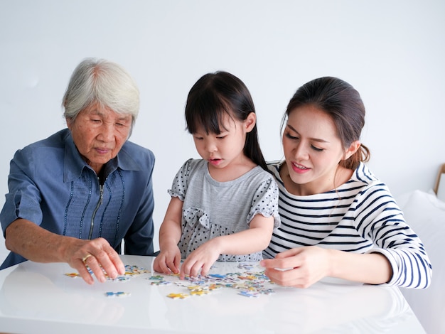 Niña jugando puzzel con su madre y su abuela en casa el fin de semana.