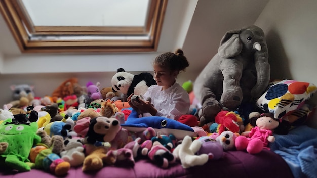 Foto niña jugando rodeada de sus peluches en la cama