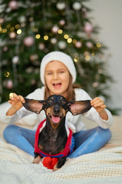 Una niña jugando con su perro cerca del árbol de Navidad.