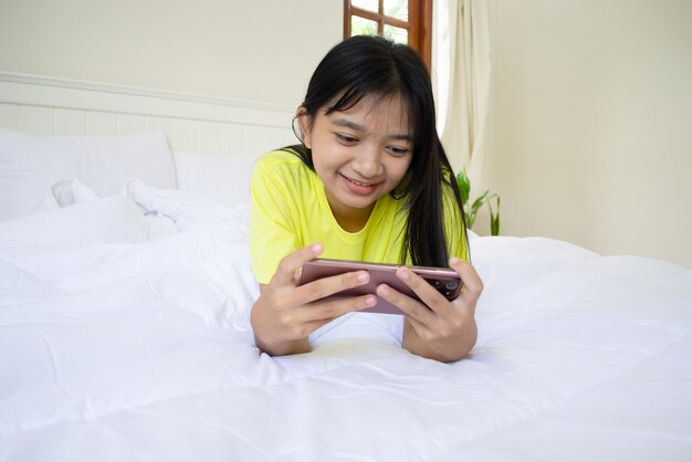 Niña jugando en el teléfono inteligente en la cama en el dormitorio en casa