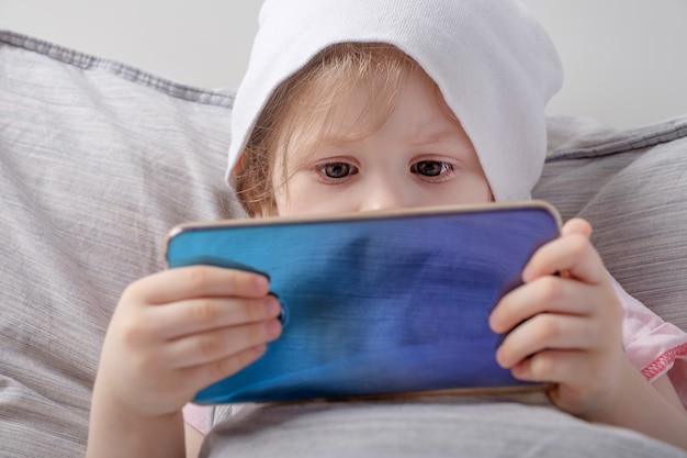 Foto niña jugando con el teléfono inteligente en la cama