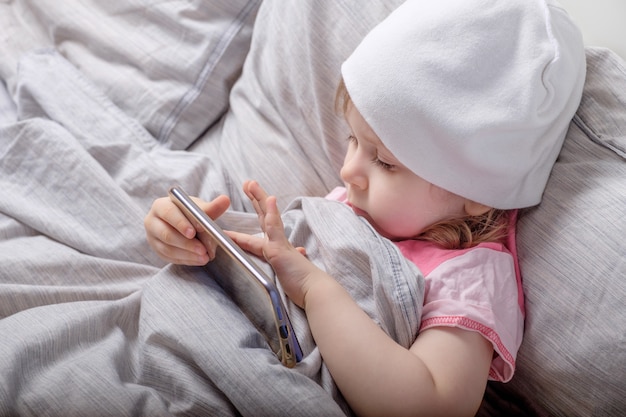 Foto niña jugando con el teléfono inteligente en la cama