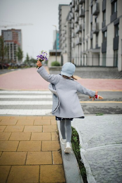 Una niña con un juguete y un abrigo gris camina por la calle.