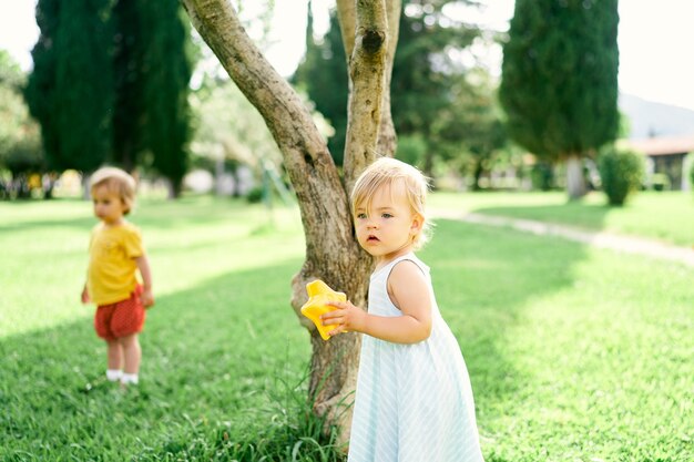 Niña con un juguete en la mano se encuentra cerca de un árbol en el parque con el telón de fondo de otro