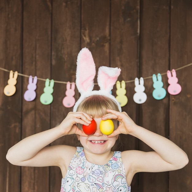 Foto niña juguetona en orejas de conejo con huevos