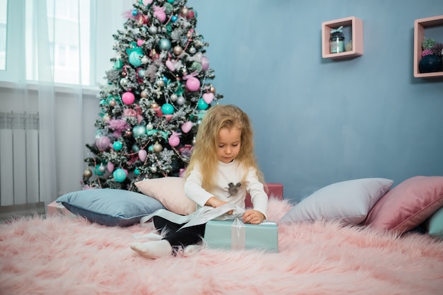 Niña juguetona se sienta en la cama y abre un regalo de Navidad