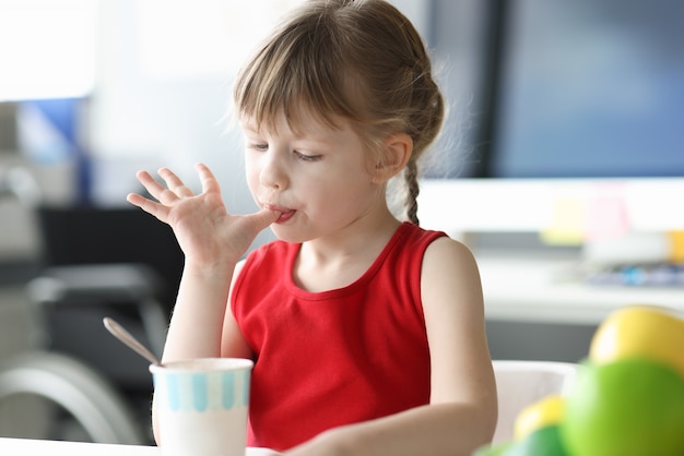 Foto niña lamiendo sus dedos delante de un vaso de helado