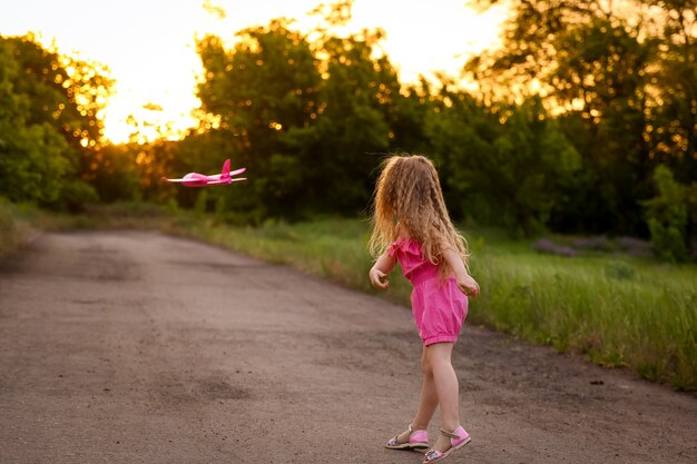 La niña lanza un avión rosa en la pared del bosque y la hierba alta