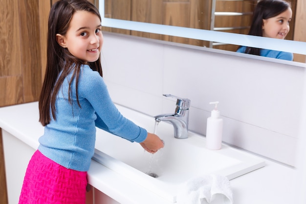 Niña se lava las manos en el baño.