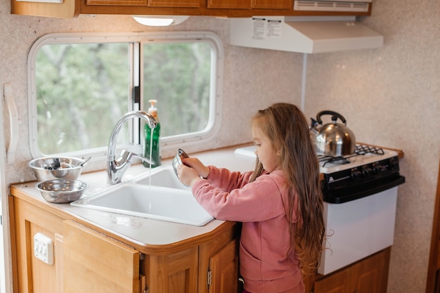 Niña lavando platos en la cocina de un remolque de viaje