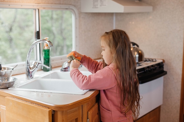 Niña lavando platos en la cocina de un remolque de viaje