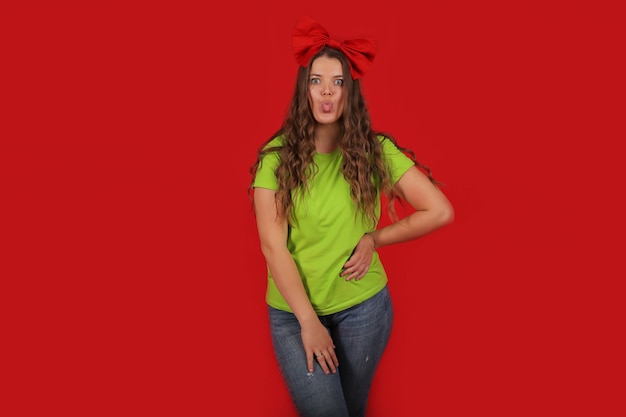 una niña con un lazo rojo en la cabeza con una camiseta verde claro con jeans azules muestra una emoción