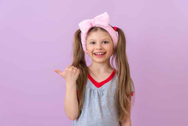 Una niña con un lazo rosa en la cabeza apunta hacia un lado.