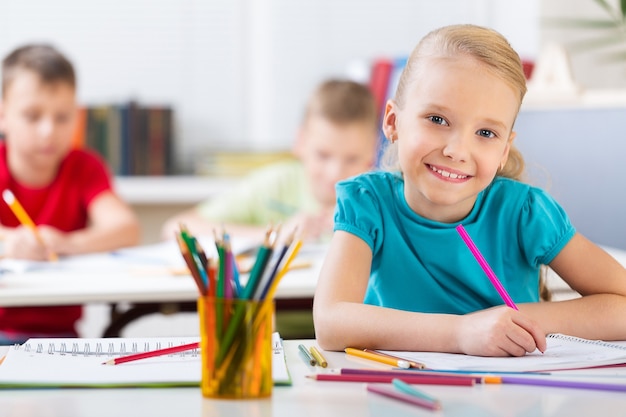 Niña en la lección de pintura en la escuela con muchachos borrosos en el fondo