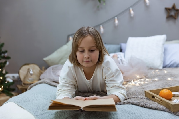 Una niña lee un libro en una cama en el dormitorio.