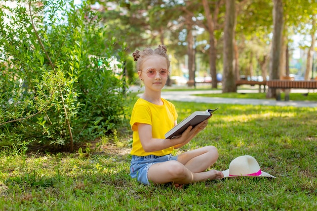 Una niña lee un libro sobre la hierba en el parque en el verano