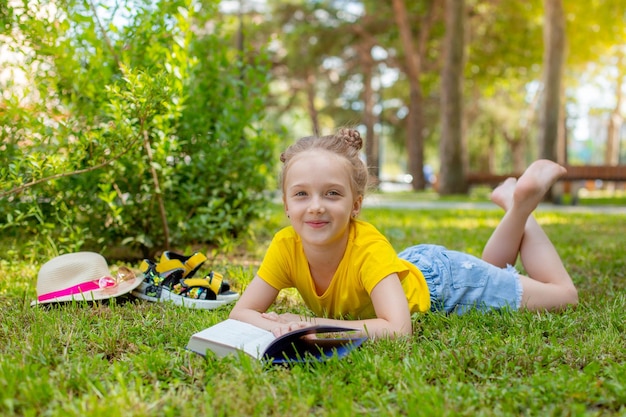 Una niña lee un libro sobre la hierba en el parque en el verano