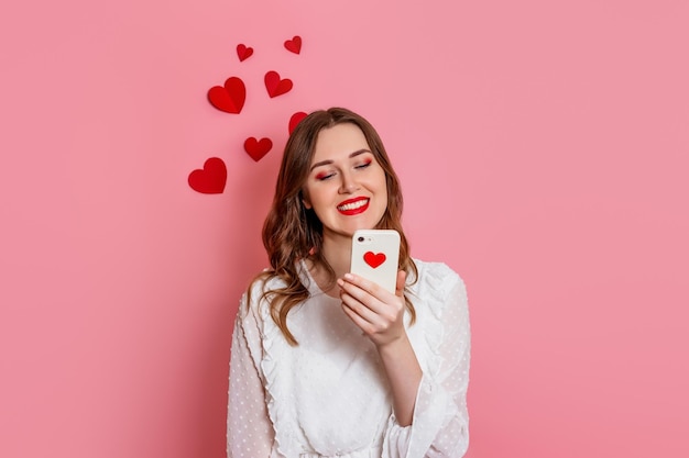 La niña lee sms de amor sonriendo sobre un fondo rosa felicitaciones por el día de san valentín