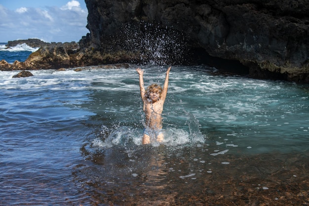 La niña levanta las manos en el agua y salpica gotas de agua en el mar Concepto de viaje y vacaciones de verano para niños