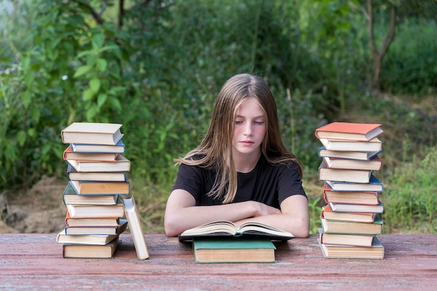 Niña leyendo un libro en el jardín en una mesa de madera con una pila de libros