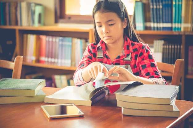 Niña leyendo un libro mientras está sentada en la mesa