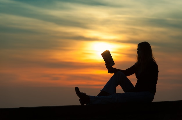 Niña leyendo un libro en la pared al atardecer