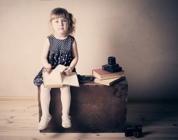 Niña leyendo un libro sobre la maleta vieja